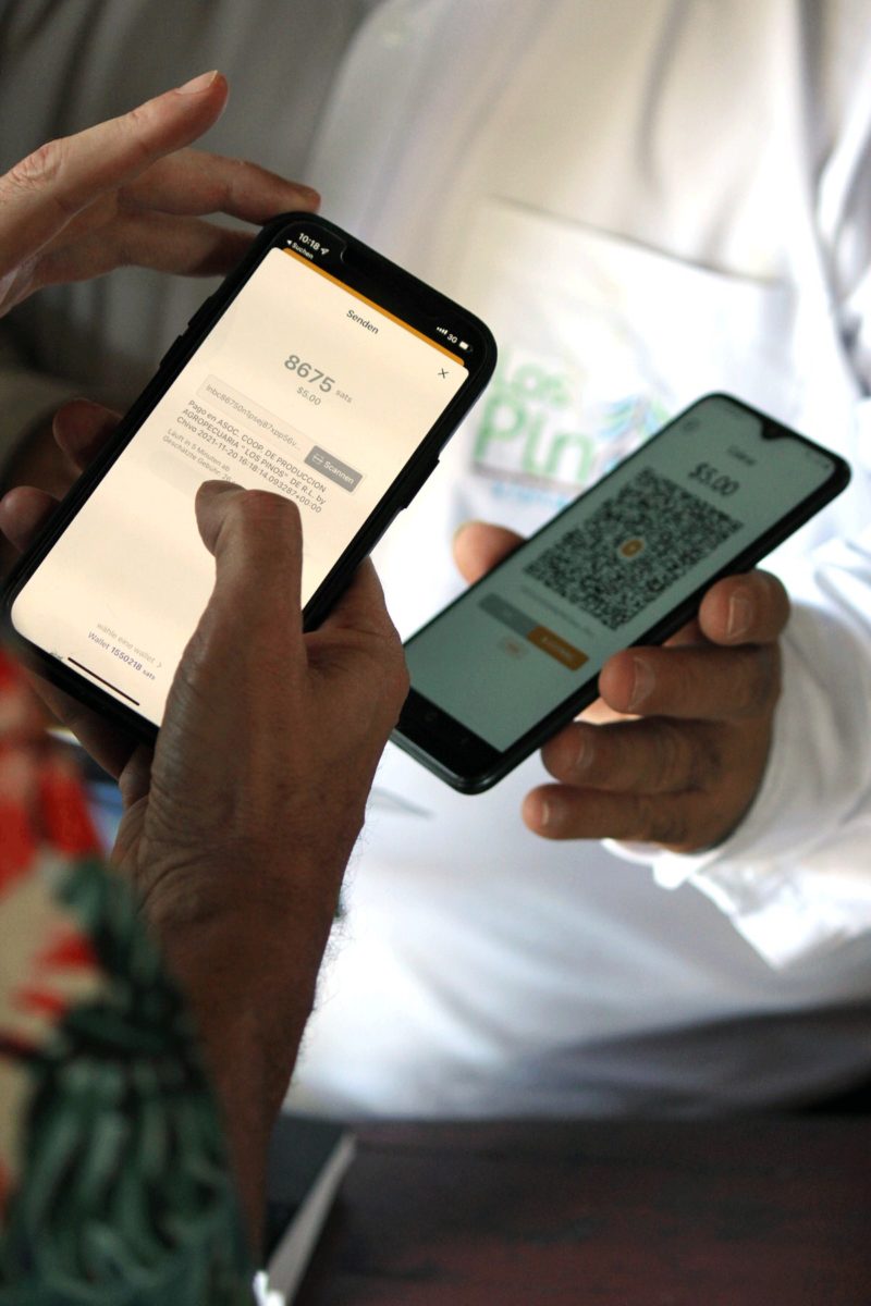 Ein Mann zeigt ein Smartphone mit einem QR-Code im Wert von 5 US-Dollar zum Bezahlen mit Bitcoin. Ein anderer scannt den Code mit der Wallet seines eigenen Handys, um die Rechnung im Wert von 8675 Satoshis zu bezahlen.