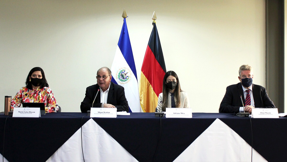 Vier salvadorianische und deutsche Vertreter aus Politik und Wirtschaft bei einer Pressekonferenz. Im Hintergrund die Flaggen von Deutschland und El Salvador.